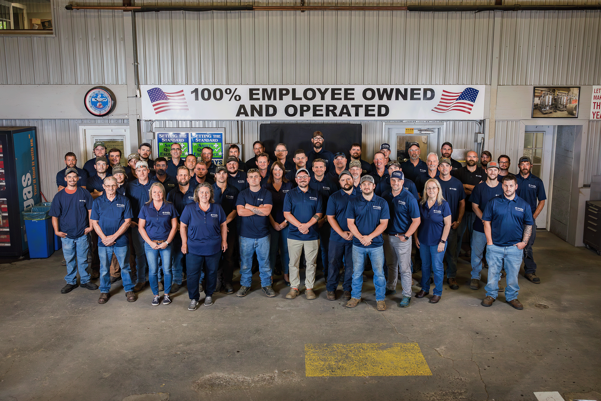 Steel Pro employees stand as a group in front of a banner that says, 100% Employee Owned and Operated